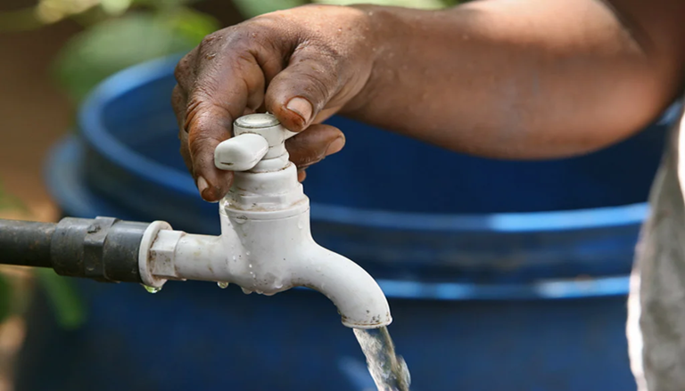 A hand opening a water faucet outside